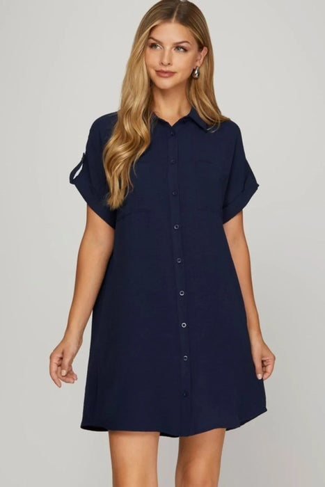 Woman wearing a navy short sleeve shirt dress with front buttons and a relaxed fit.