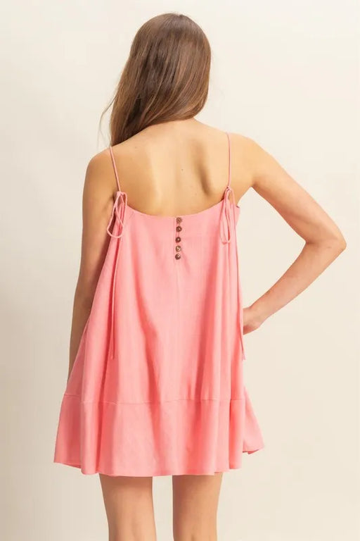 Back view of a pink swing mini dress featuring spaghetti straps with tie details and decorative buttons along the upper back