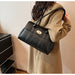Black leather shoulder tote bag with gold twist lock clasp, styled on a model wearing a tan blazer