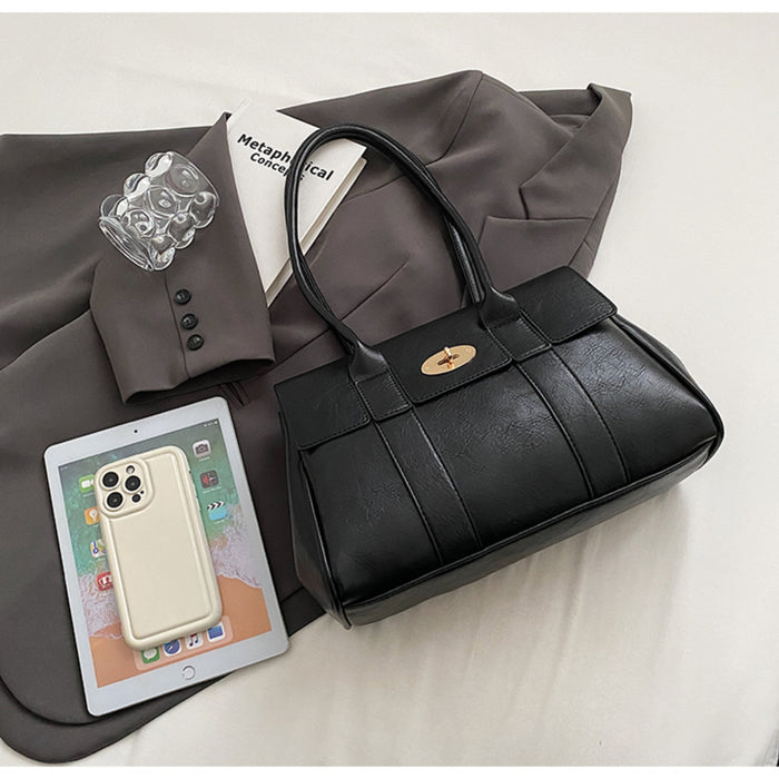 Black leather top handle tote bag with gold twist lock closure, styled on a grey blazer next to a tablet and accessories.