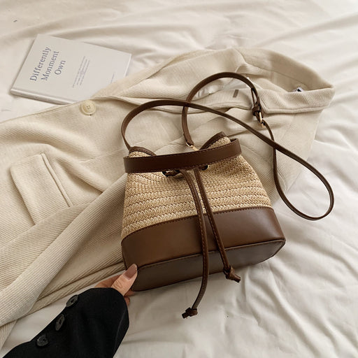 Chic woven bucket bag with brown leather details and drawstring closure, styled on a beige coat for a cozy, elegant vibe.