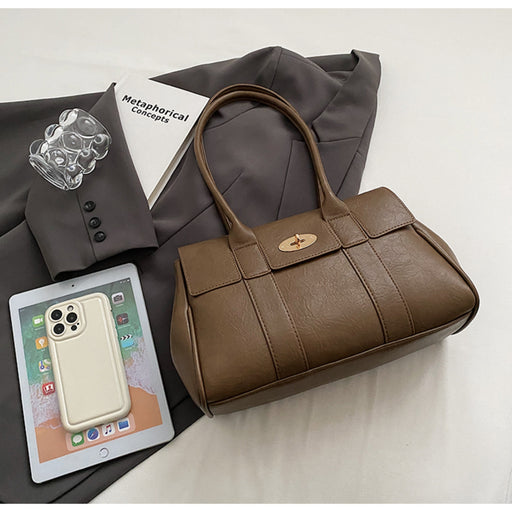 "Brown leather handbag with gold turn-lock placed on a gray blazer, next to a tablet and accessories, showcasing a stylish flat lay
