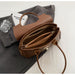 Top view of an elegant brown leather shoulder bag showcasing multiple zippered compartments, placed on a grey suit with a minimal aesthetic.