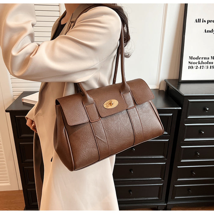 Dark brown leather handbag with gold turn-lock clasp worn on shoulder, paired with a beige blazer for a chic and professional look.
