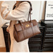 Dark brown leather handbag with gold turn-lock clasp worn on shoulder, paired with a beige blazer for a chic and professional look.