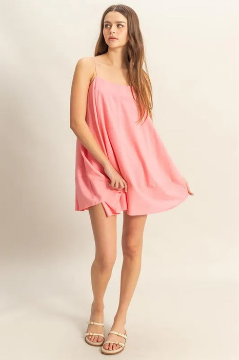 Front view of a woman wearing a sleeveless flowy pink mini dress with spaghetti straps, styled with white sandals