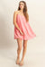 Front view of a woman wearing a sleeveless flowy pink mini dress with spaghetti straps, styled with white sandals