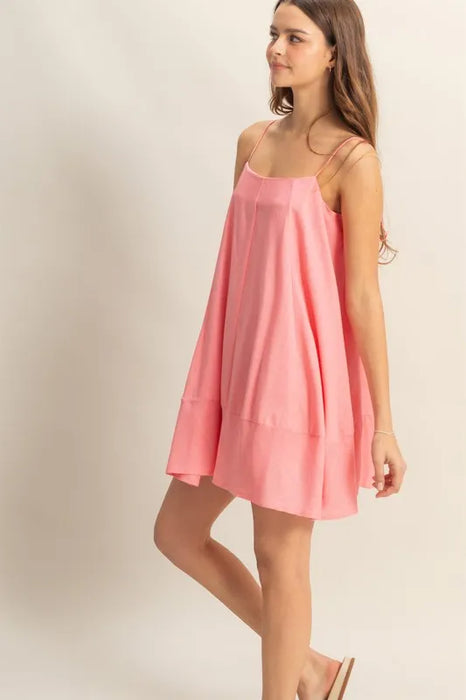 Side view of a woman wearing a light pink swing mini dress with spaghetti straps and a flowy silhouette