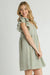 Smiling woman in a tan and blue plaid babydoll dress with ruffled sleeves, showing a side profile with flowing skirt