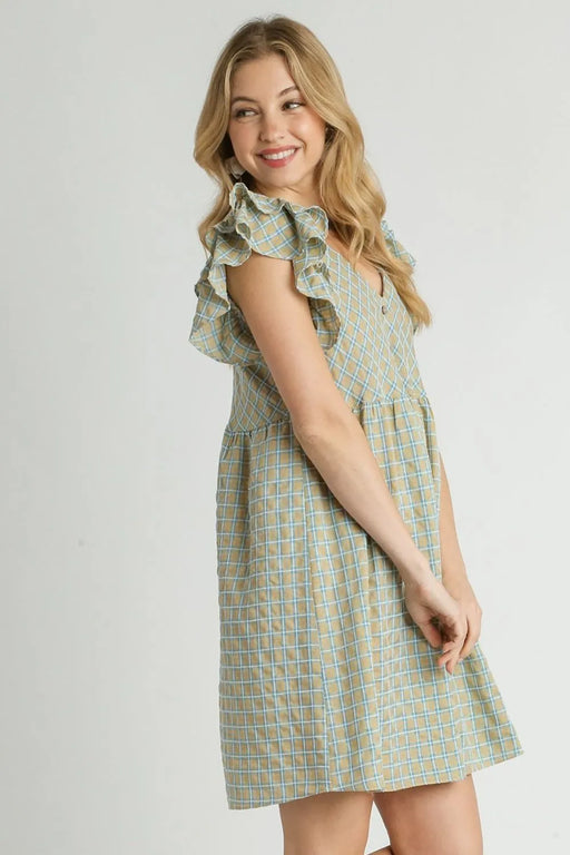 Smiling woman in a tan and blue plaid babydoll dress with ruffled sleeves, showing a side profile with flowing skirt