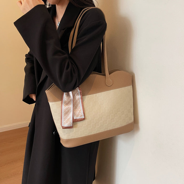 Model wearing a tan checkered tote bag with brown leather accents and silk scarf detail, styled with a black coat