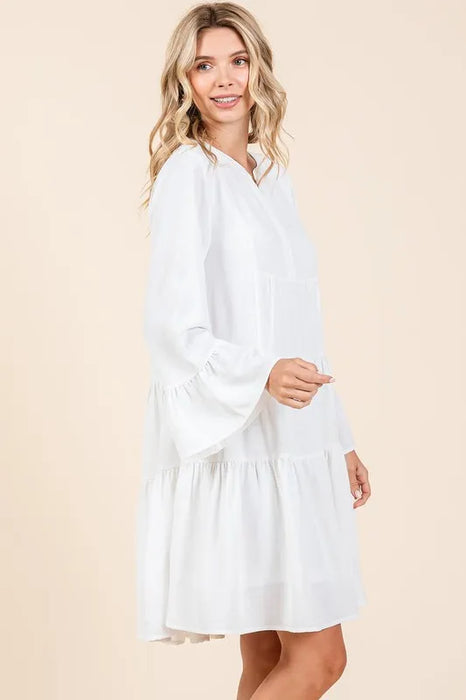 Side view of a smiling woman wearing a white boho-style tiered dress with long flared sleeves, ideal for spring and summer fashion
