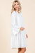Side view of a smiling woman wearing a white boho-style tiered dress with long flared sleeves, ideal for spring and summer fashion